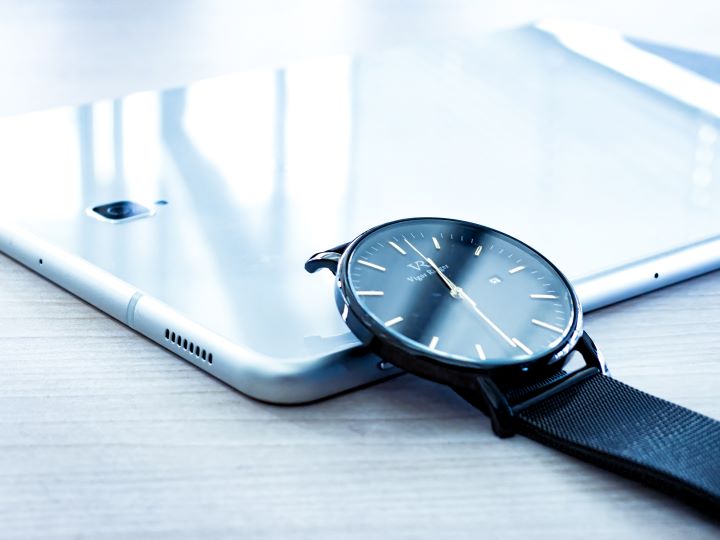 A tablet lays facedown on a table with a wristwatch leaning on top of it